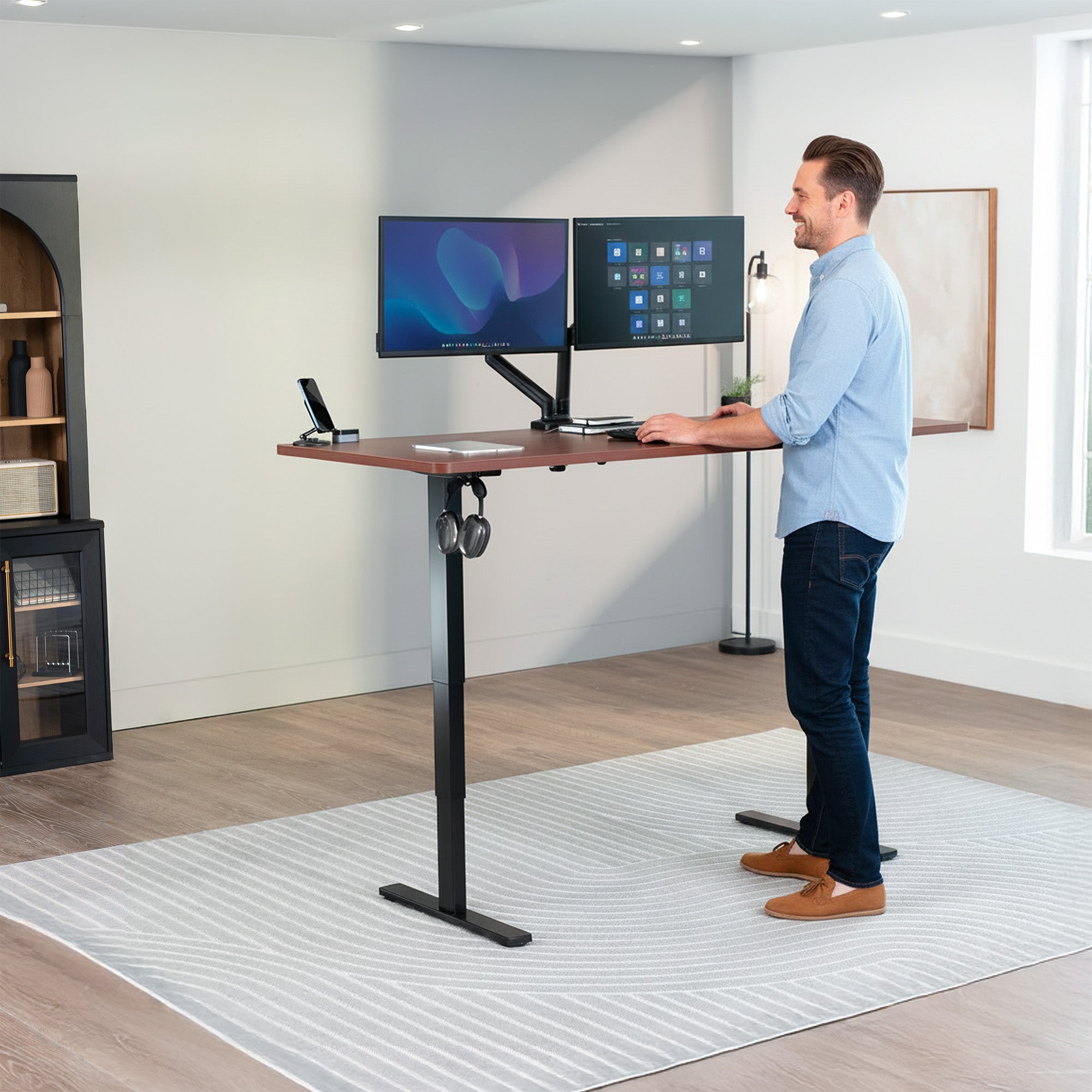 Man using a standing desk with two monitors in a home office setting.