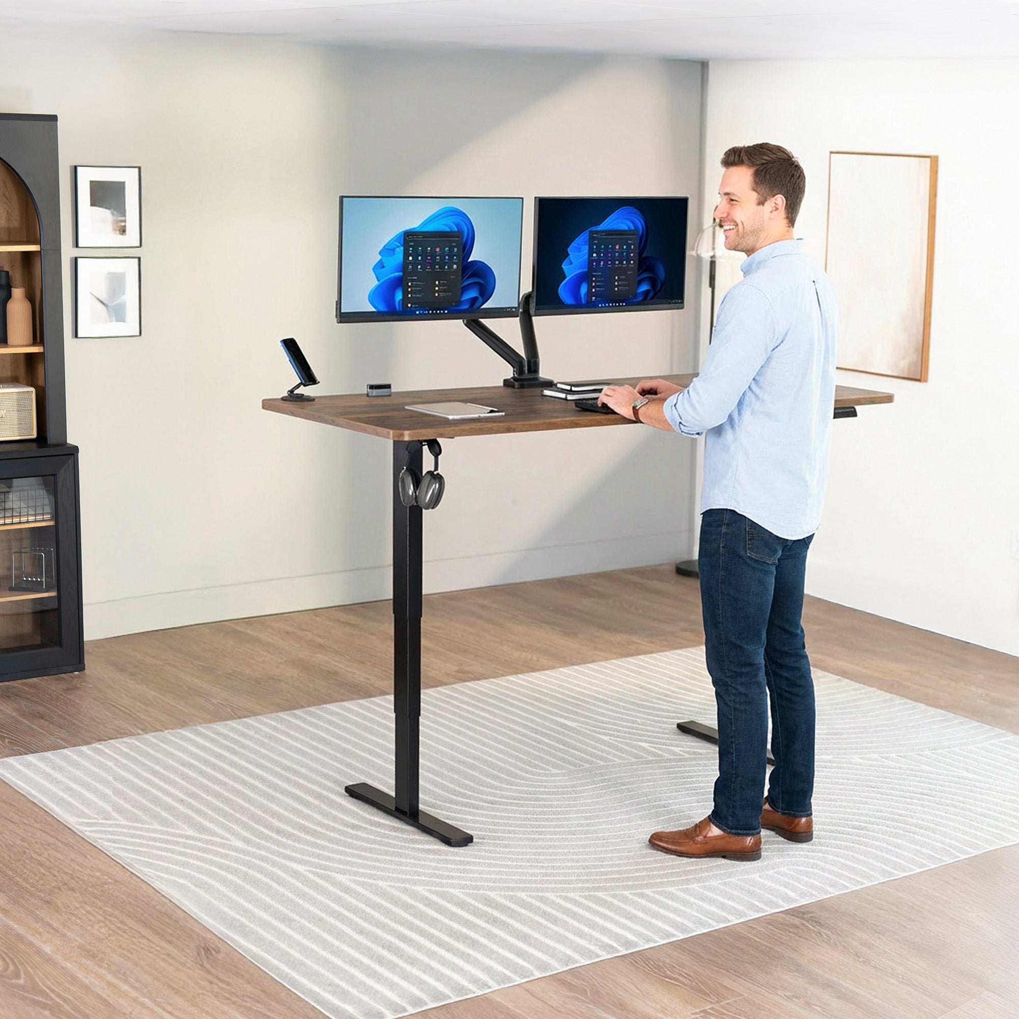 Man using a standing desk with dual monitors in an office setting.
