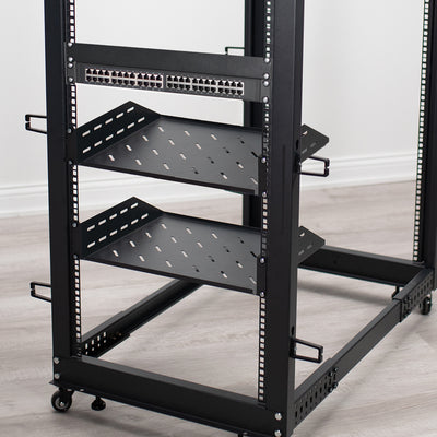 Black metal server rack with shelves on a wooden floor.