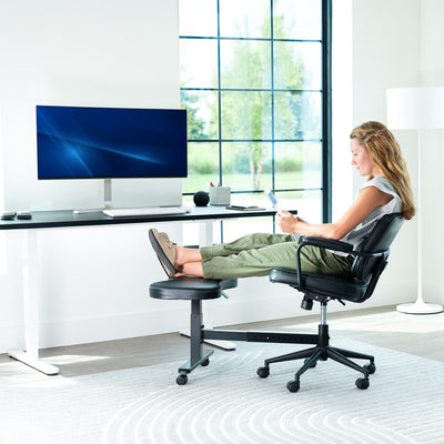 Person sitting at a desk with feet propped up on a footrest in a modern office setting