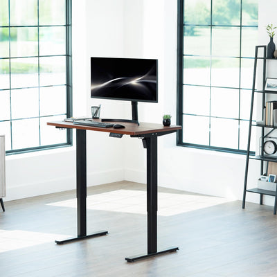 Adjustable height desk with a computer setup in a bright room with large windows.