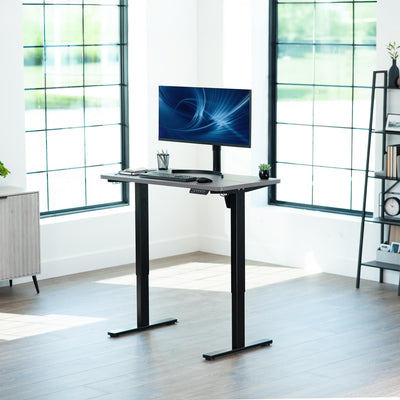 Modern office setup with a standing desk and computer monitor in a bright room.