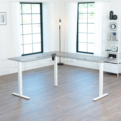 Modern L-shaped white desk frame in a bright room with large windows.
