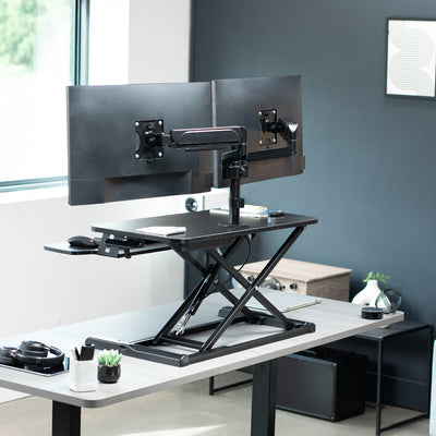 Height adjustable desk riser with articulating pneumatic dual monitor mount.