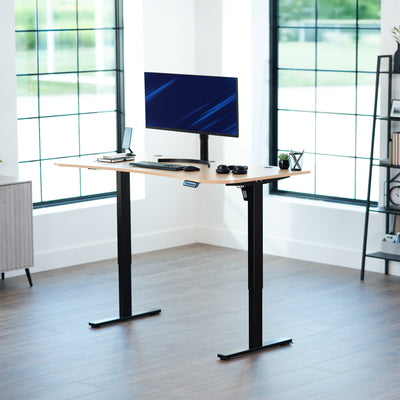 Light wood, electric, sit to stand, height adjustable desk in office setting.