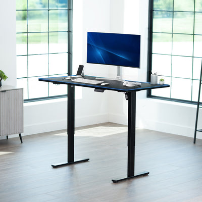 Modern office setup with a standing desk with full-size RGB pad with a freestanding computer monitor in a bright room.