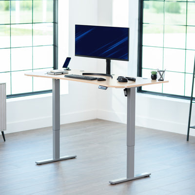 Light wood top grey frame, electric, sit to stand, height adjustable desk in office setting.