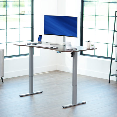 Dark walnut top grey frame, electric, sit to stand, height adjustable desk in office setting.