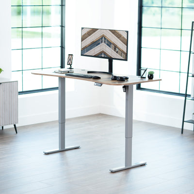 Reclaimed wood top grey frame, electric, sit to stand, height adjustable desk in office setting.