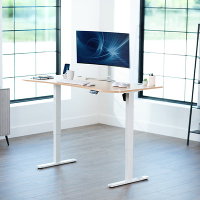 Light wood top white frame, electric, sit to stand, height adjustable desk in office setting.