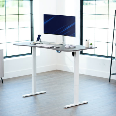 Dark grey top white frame, electric, sit to stand, height adjustable desk in office setting.