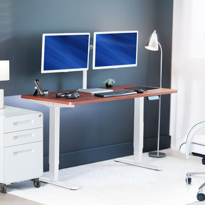 Modern office desk with two computer monitors, keyboard, and lamp against a gray wall.