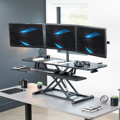 Spacious height adjustable desk riser with articulating triple monitor mount.