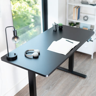 Black adjustable desk with office items in a bright room