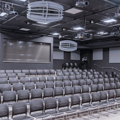 A large oval-shaped acoustic ceiling sound absorber in a light gray color in a auditorium setting. 