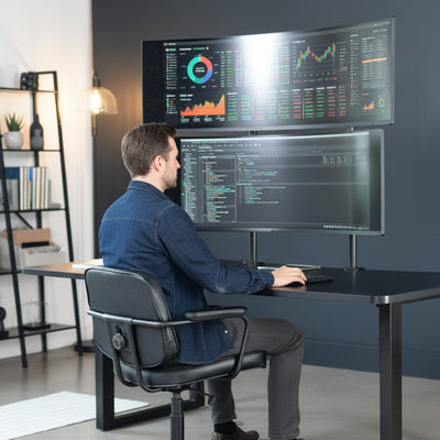 Man sitting at a desk with multiple computer monitors displaying financial data.