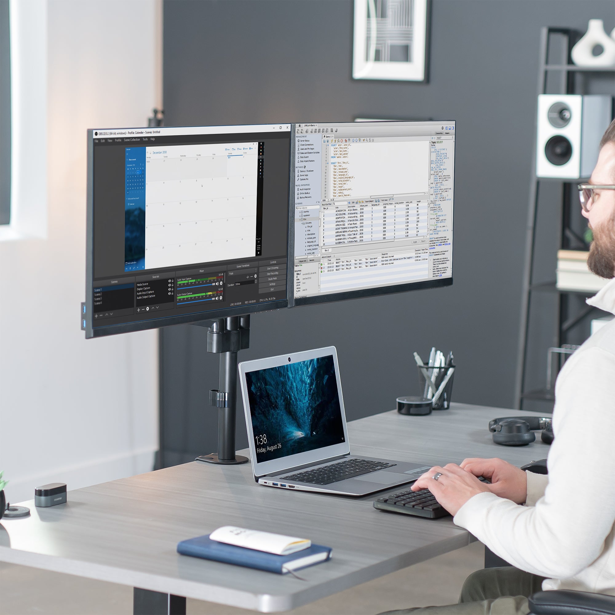 Model typing at desk with laptop and dual monitor stand.