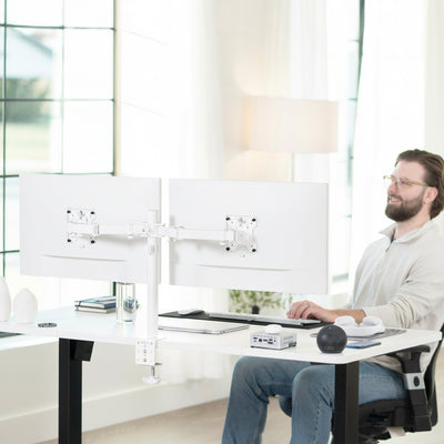 Man sitting at a modern desk with dual monitors attached to dual monitor desk mount in a bright office setting
