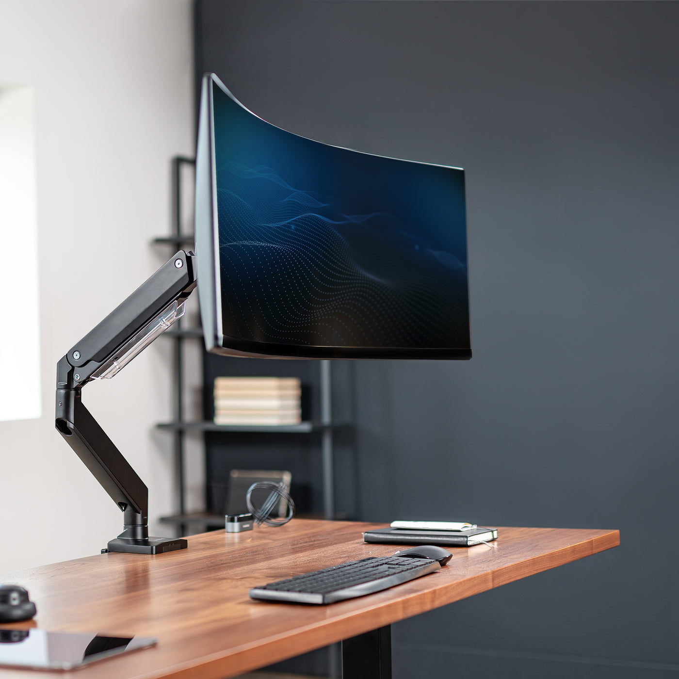 Sturdy arm clamped onto a desk supporting a curved monitor in an aesthetic office.