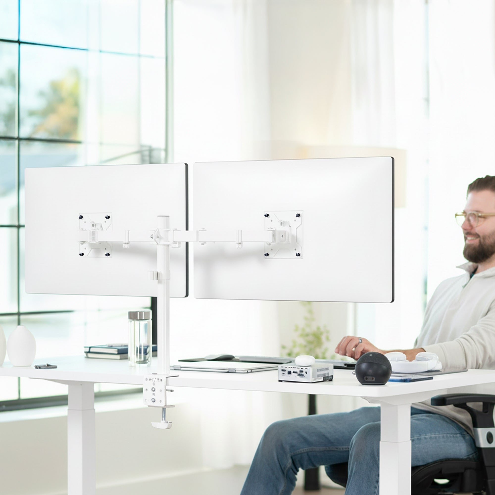 Person using a computer with dual monitors on a white desk in a bright office setting