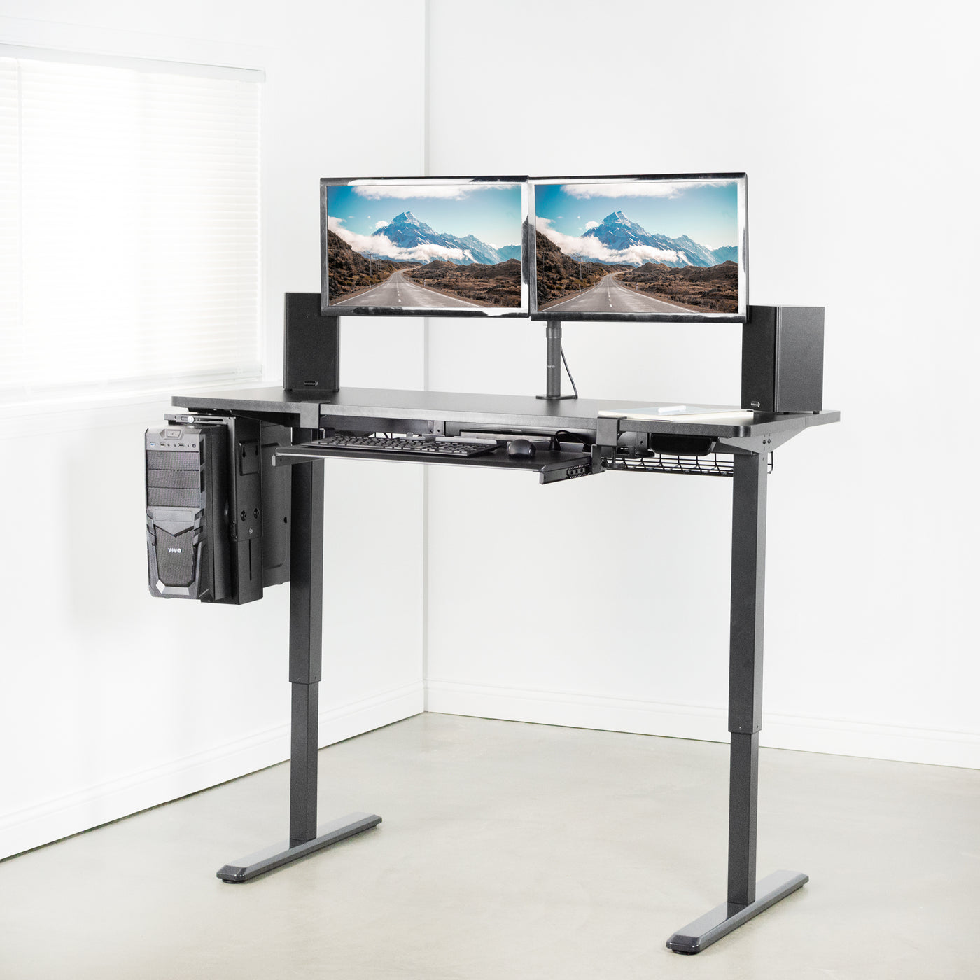 Standing electric desk, supporting under desk PC, cable management net, speaker, and dual monitor mount with under desk sliding keyboard tray.
