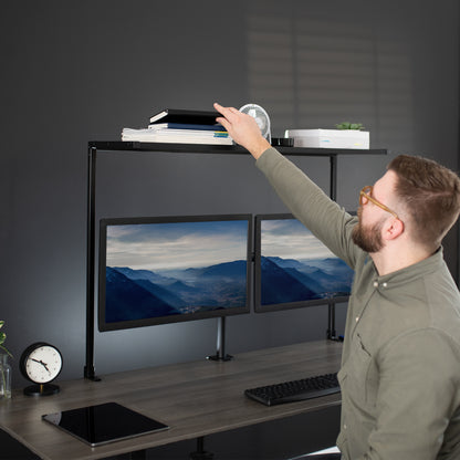 A man pulling a book off of an overhead clamp on a desk shelf.