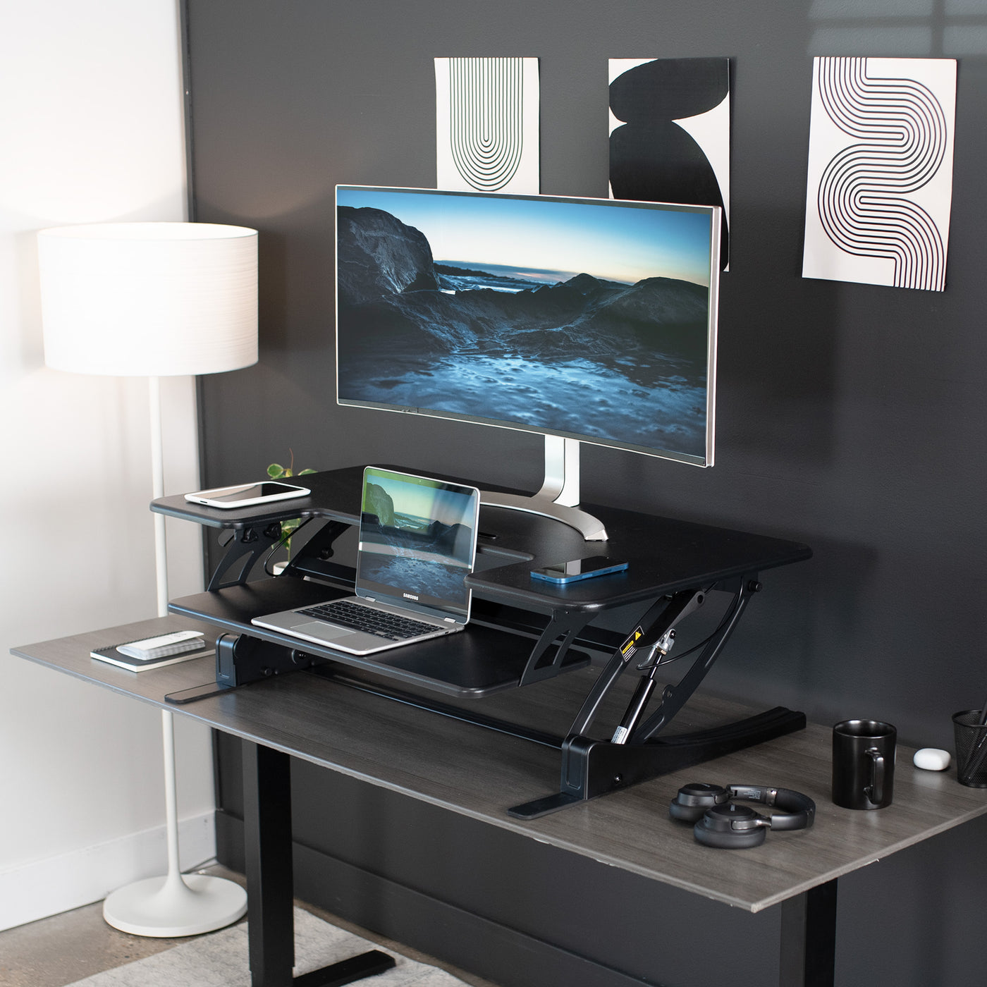 Modern desk riser on an office desk top holding several devices. 