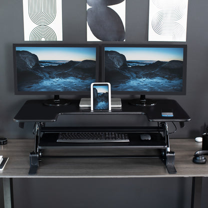 Desk converter in use with two monitors with device propped up in designated device holder slot.