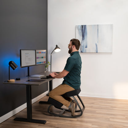 A man using a kneeling chair while working at a modern office desk.