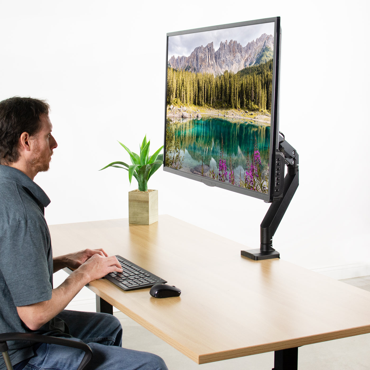Man working at a desk with an extra large mounted monitor. 