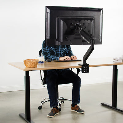 A man working at a desk with a large tv monitor and sturdy VESA plate.