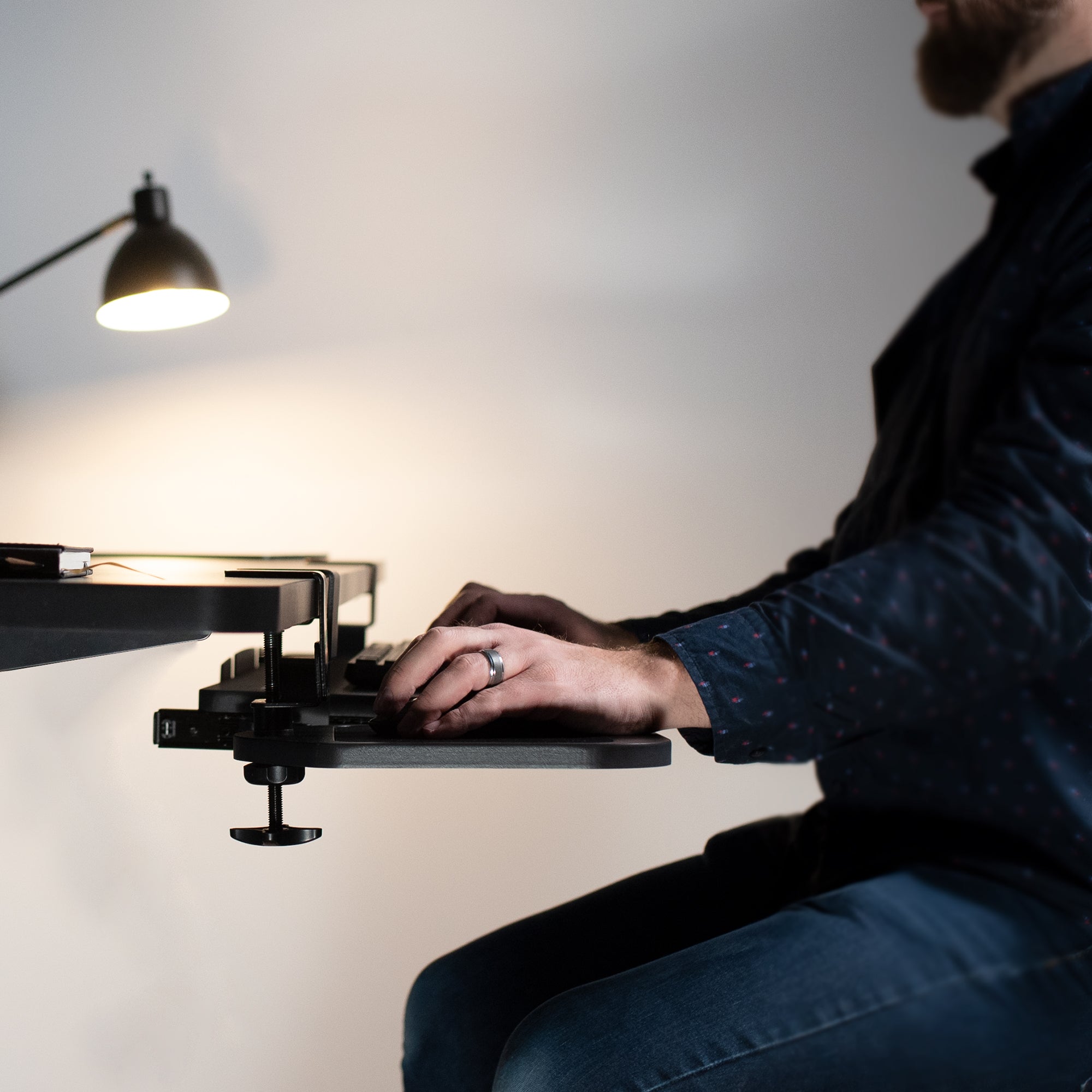 A man sitting and working from a desk with a pull-out keyboard tray and clamp-on mouse tray.