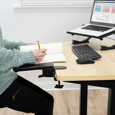 Clamp on desk stays in use with a person taking notes on a notebook.