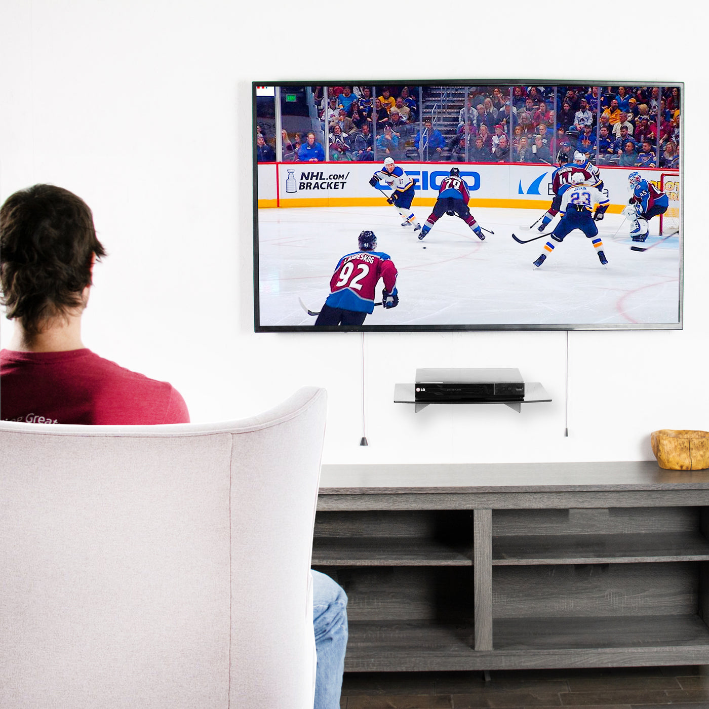 A man watching a hockey game with a floating shelf supporting an LG TV.