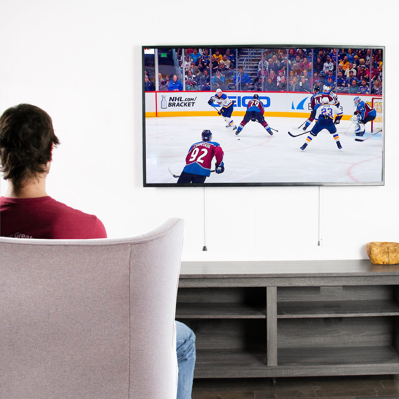 A man watching hockey on an extra large TV mounted to the wall.