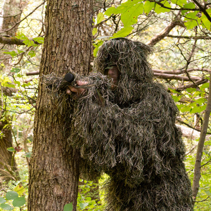 Man in a ghillie suit blending into the outdoor environment.