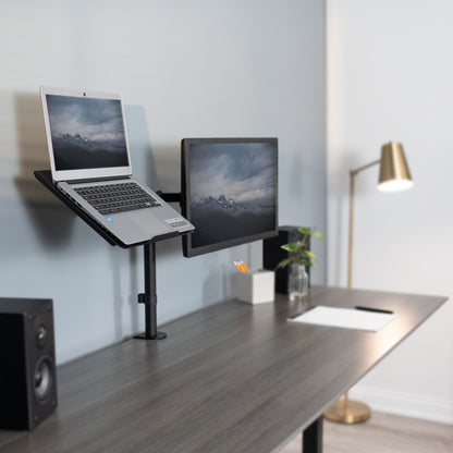 A laptop stands on the same pole as a single monitor mount holding the laptop screen and monitor screen at similar levels.