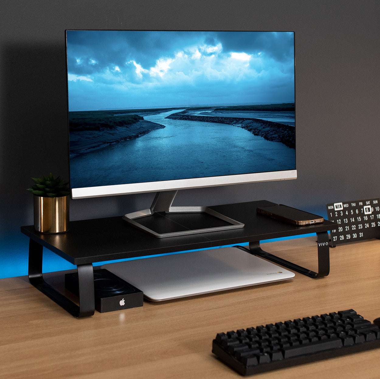 An elevated monitor on top of a desk riser with a laptop and phone stored underneath in the extra space.